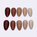 Nine almond-shaped false nail tips arranged in two rows on a light gray background, showing a gradient of colors from deep burgundy and warm brown to light beige and nude.