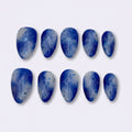 A set of ten blue press-on nails with white marble or cloudy patterns, arranged in two rows of five on a plain light gray background.