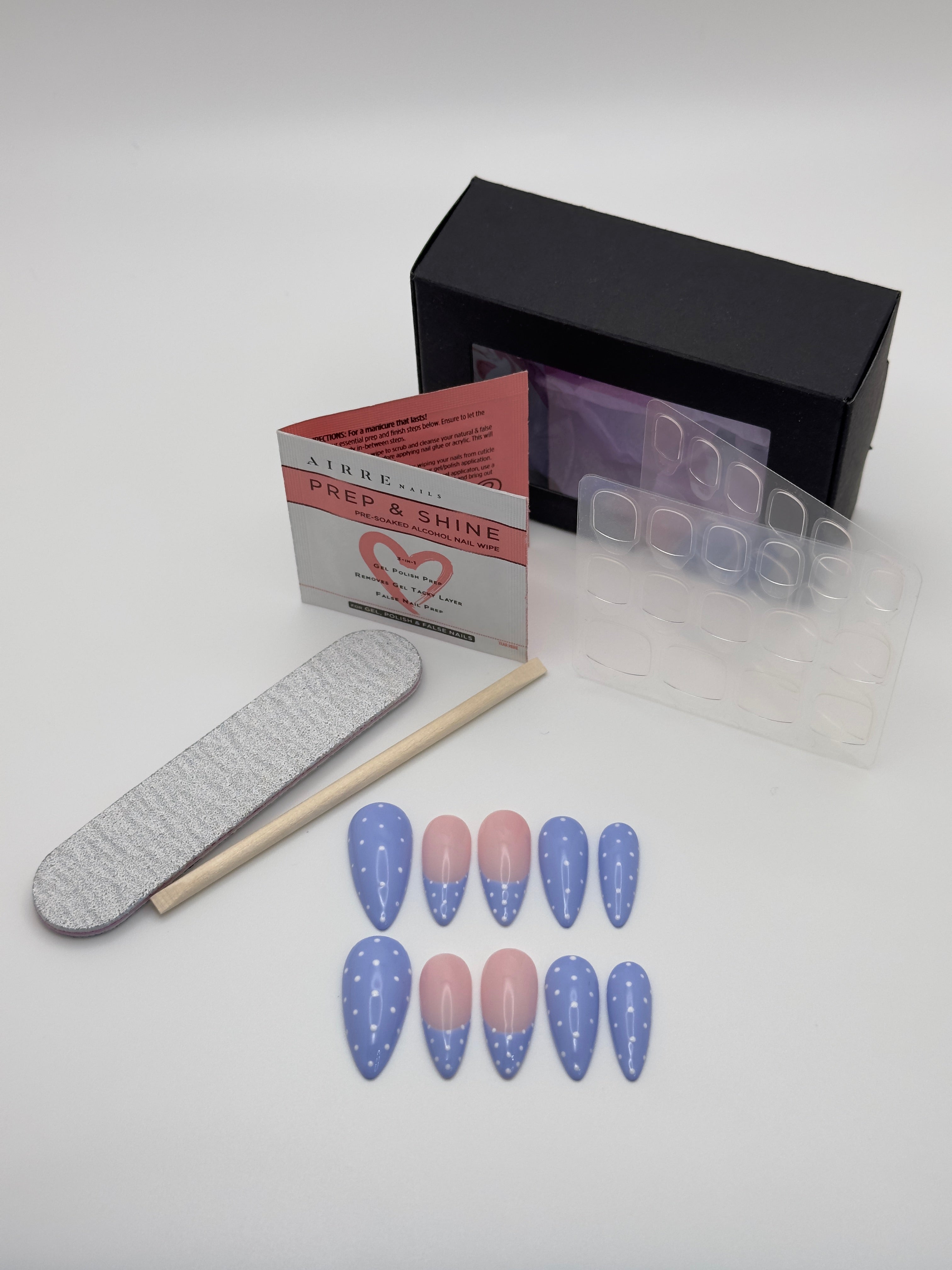 A nail art kit on a light gray background, including a black box, a Prep Shine card, a gray nail file, a wooden nail stick, a clear tray of press-on nail templates, and ten false nails with a blue-to-pink gradient and white star pattern.
