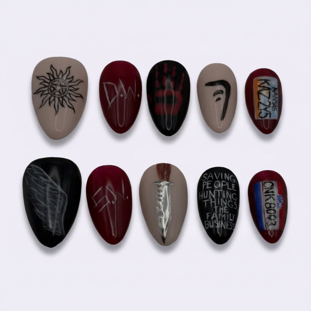 A set of ten custom nail art press-on nails arranged in two rows of five on a plain light gray background. The designs include black and red gothic symbols, white gothic lettering, and a small multicolor graphic.