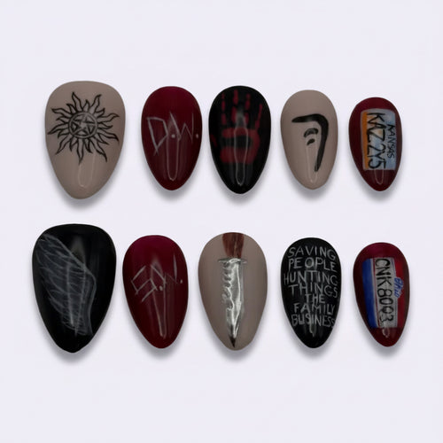 A set of ten custom nail art press-on nails arranged in two rows of five on a plain light gray background. The designs include black and red gothic symbols, white gothic lettering, and a small multicolor graphic.
